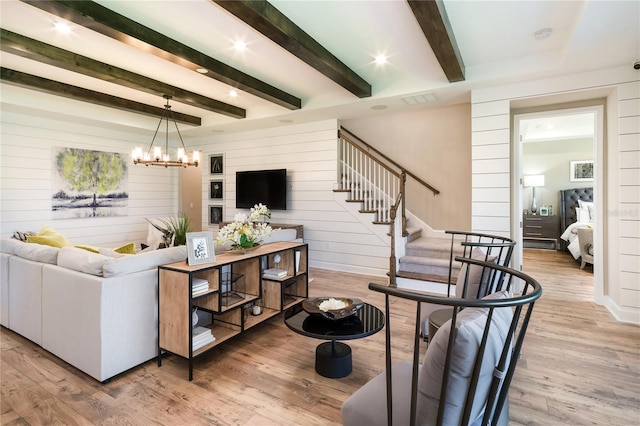 living room with wood walls, an inviting chandelier, beam ceiling, and light hardwood / wood-style flooring