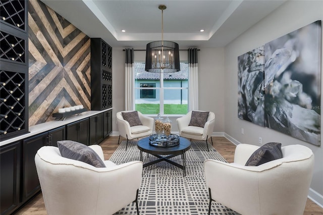 living area with a raised ceiling, light hardwood / wood-style floors, and a notable chandelier