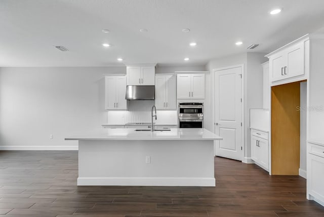 kitchen with dark wood-style floors, baseboards, recessed lighting, under cabinet range hood, and double oven