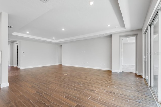 unfurnished living room with baseboards, wood finished floors, a tray ceiling, and recessed lighting