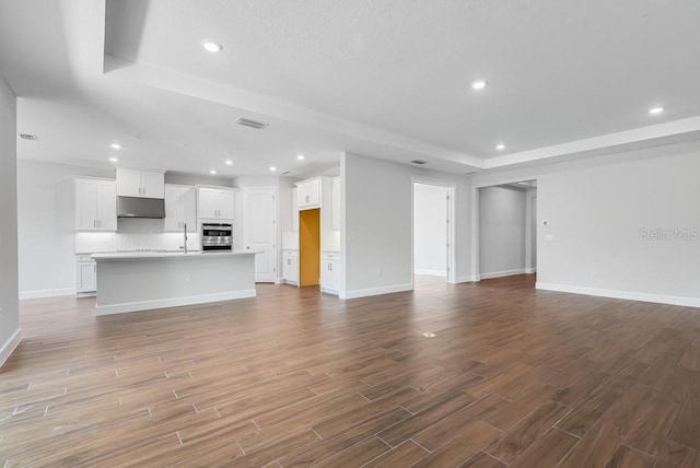 unfurnished living room featuring recessed lighting, a raised ceiling, visible vents, dark wood-type flooring, and baseboards