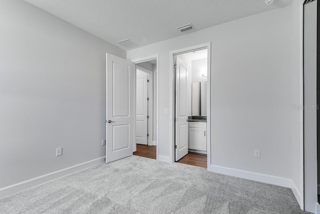 unfurnished bedroom featuring visible vents, baseboards, ensuite bathroom, and carpet flooring