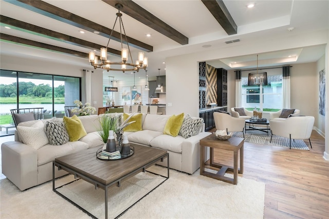 living room with an inviting chandelier, light hardwood / wood-style flooring, and beamed ceiling