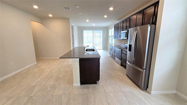 kitchen with sink, dark brown cabinetry, appliances with stainless steel finishes, an island with sink, and light stone counters