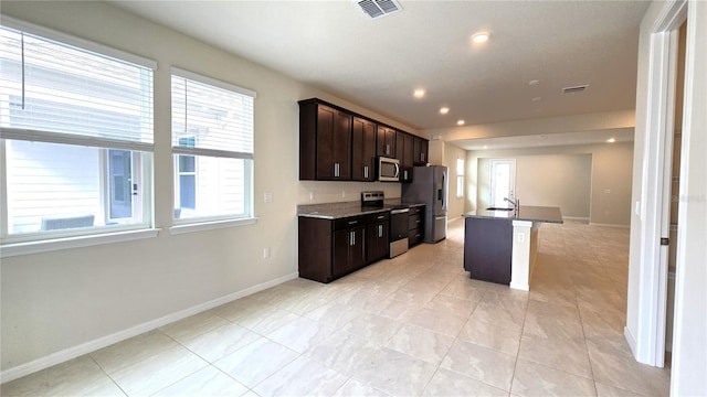 kitchen featuring a kitchen bar, stainless steel appliances, stone countertops, a kitchen island with sink, and dark brown cabinets