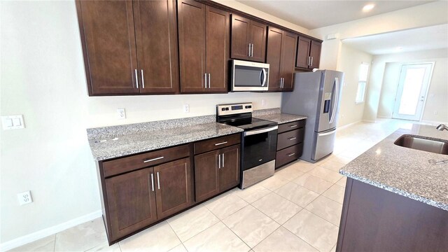 kitchen featuring light stone countertops, appliances with stainless steel finishes, sink, and dark brown cabinetry