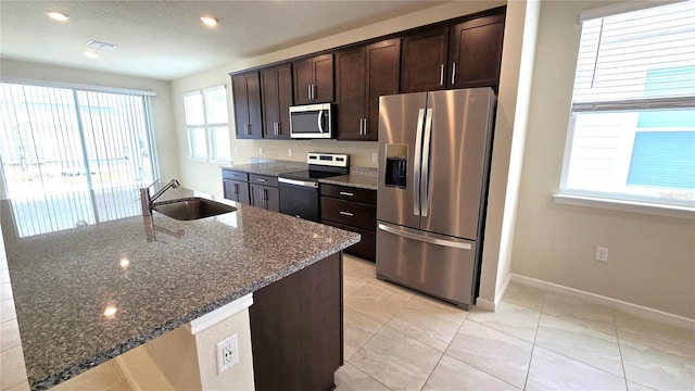 kitchen with sink, appliances with stainless steel finishes, dark brown cabinets, and dark stone counters