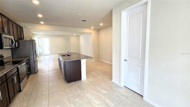 kitchen with appliances with stainless steel finishes, dark stone countertops, sink, a center island with sink, and dark brown cabinets