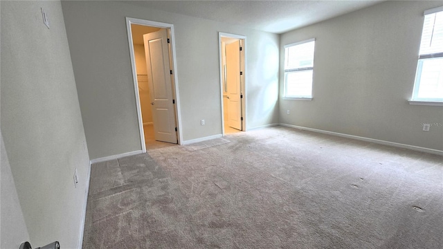 unfurnished bedroom featuring ensuite bath, multiple windows, and light carpet