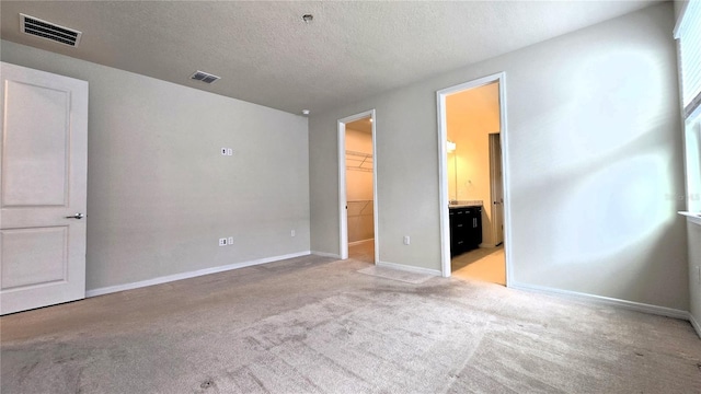 unfurnished bedroom featuring light carpet, connected bathroom, a closet, a textured ceiling, and a walk in closet