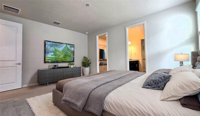 carpeted bedroom featuring a spacious closet, a textured ceiling, and ensuite bathroom