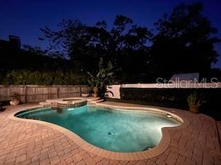 pool at night with a patio and an in ground hot tub