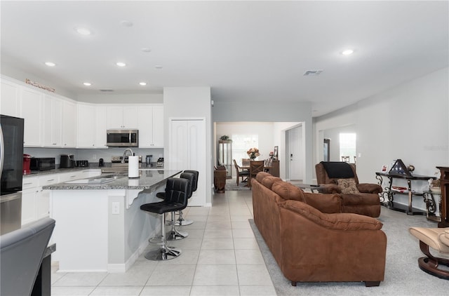 interior space featuring white cabinetry, dark stone counters, a kitchen breakfast bar, light tile patterned flooring, and a center island with sink