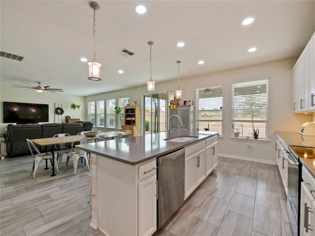 kitchen featuring sink, stainless steel appliances, a center island with sink, and white cabinetry