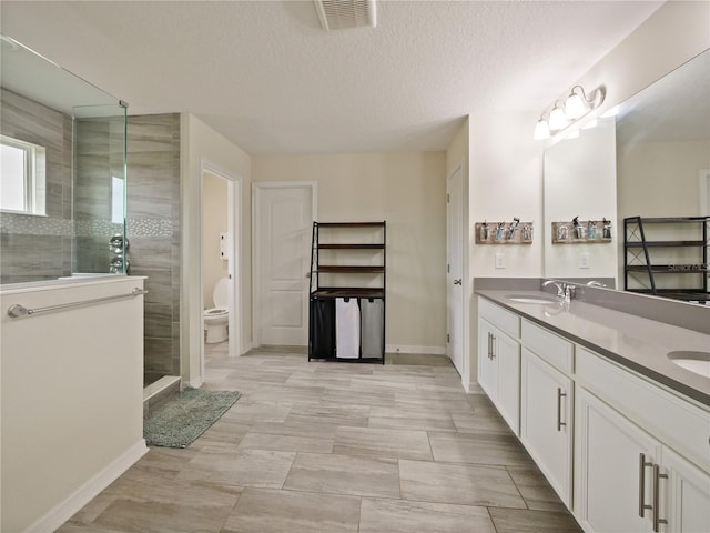 bathroom featuring toilet, a tile shower, vanity, and a textured ceiling