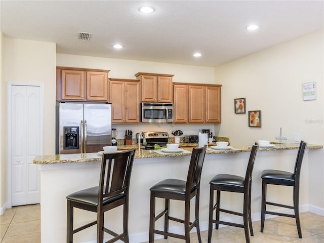 kitchen featuring a breakfast bar, appliances with stainless steel finishes, light tile patterned floors, and light stone counters