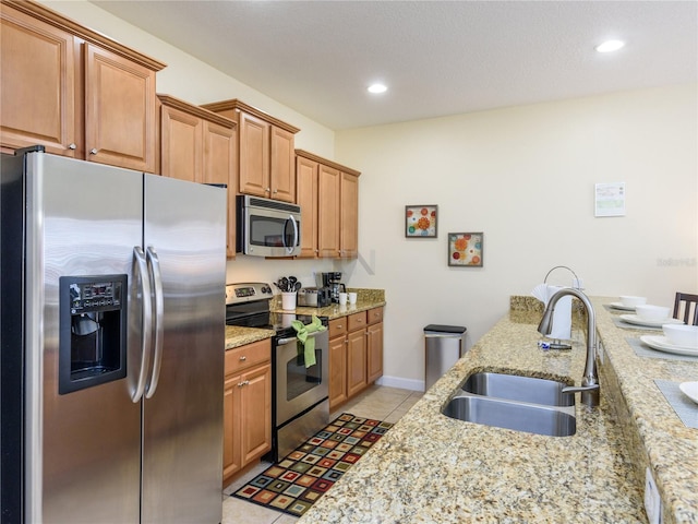 kitchen with light tile patterned floors, sink, light stone counters, and stainless steel appliances