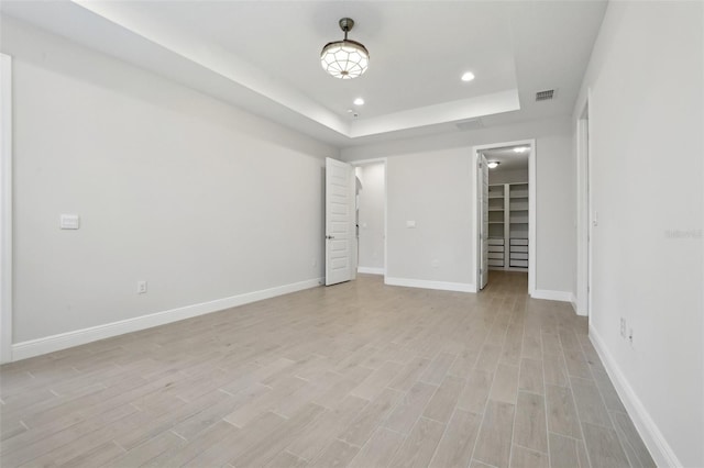 unfurnished room with a tray ceiling and light wood-type flooring