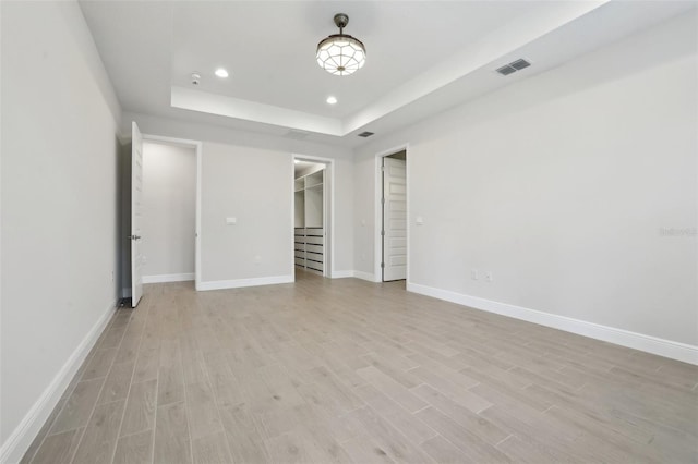 unfurnished bedroom featuring a raised ceiling, a closet, a spacious closet, and light hardwood / wood-style flooring