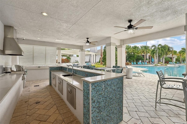 view of patio / terrace featuring ceiling fan, an outdoor kitchen, a community pool, and a wet bar