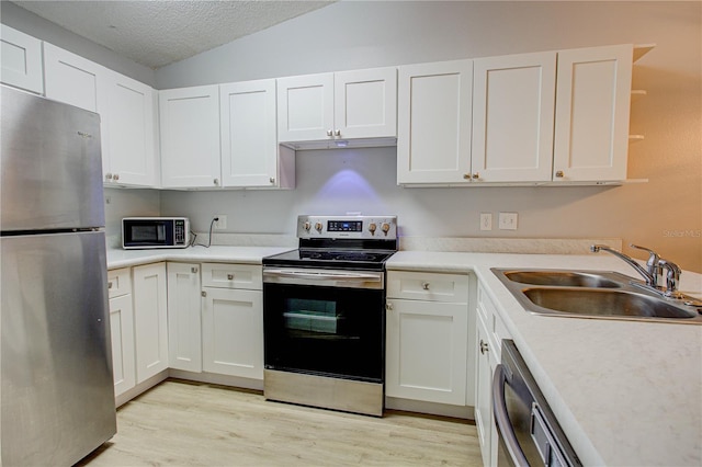 kitchen featuring stainless steel appliances, vaulted ceiling, a textured ceiling, white cabinets, and sink