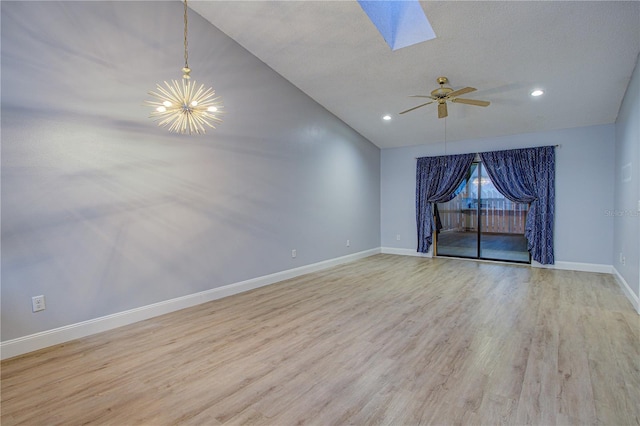 unfurnished room with lofted ceiling with skylight, ceiling fan with notable chandelier, a textured ceiling, and light hardwood / wood-style flooring