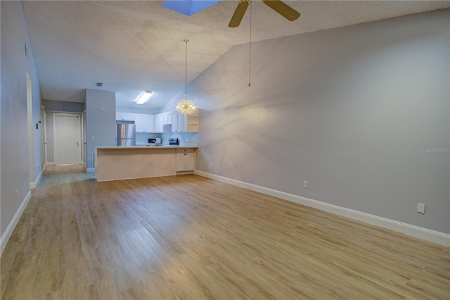 unfurnished living room featuring a textured ceiling, ceiling fan with notable chandelier, lofted ceiling, and light hardwood / wood-style floors