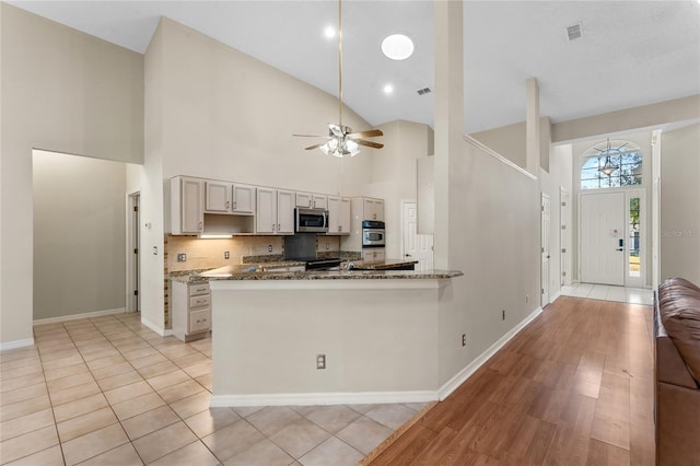 kitchen with appliances with stainless steel finishes, stone counters, light tile patterned floors, ceiling fan, and high vaulted ceiling