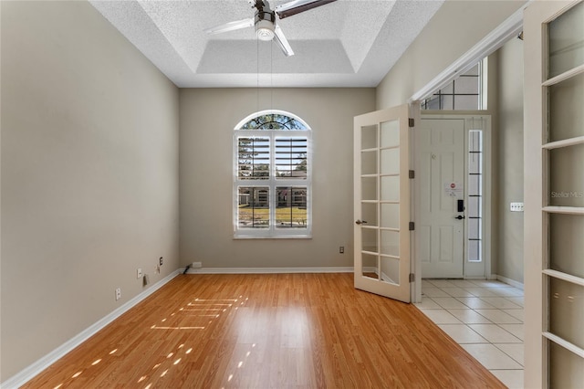 interior space featuring a textured ceiling, ceiling fan, light wood-type flooring, and a raised ceiling