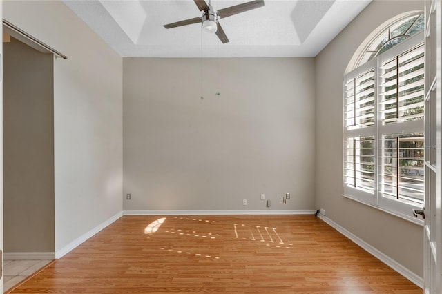 spare room featuring a textured ceiling, ceiling fan, light hardwood / wood-style floors, and a raised ceiling