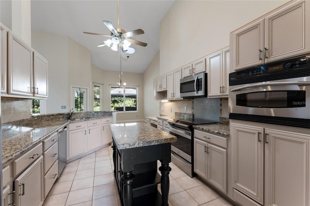 kitchen with appliances with stainless steel finishes, light tile patterned floors, light stone counters, high vaulted ceiling, and a kitchen island