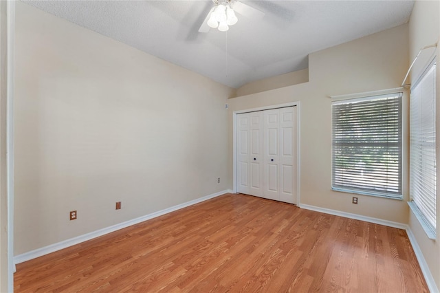 unfurnished bedroom with a textured ceiling, vaulted ceiling, a closet, light wood-type flooring, and ceiling fan