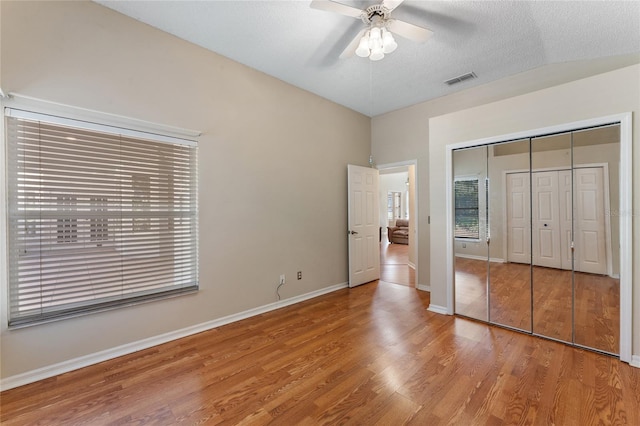 unfurnished bedroom featuring a textured ceiling, lofted ceiling, hardwood / wood-style floors, ceiling fan, and a closet