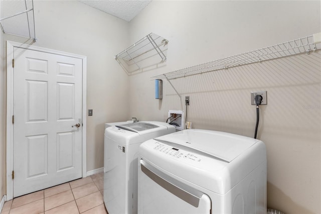 washroom with a textured ceiling, independent washer and dryer, and light tile patterned floors