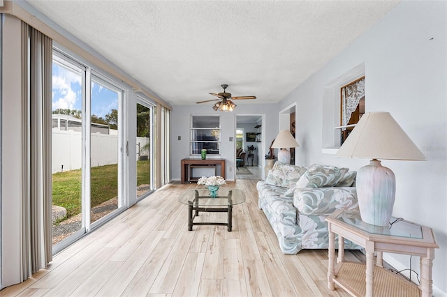 living room with a textured ceiling, ceiling fan, and light wood-type flooring