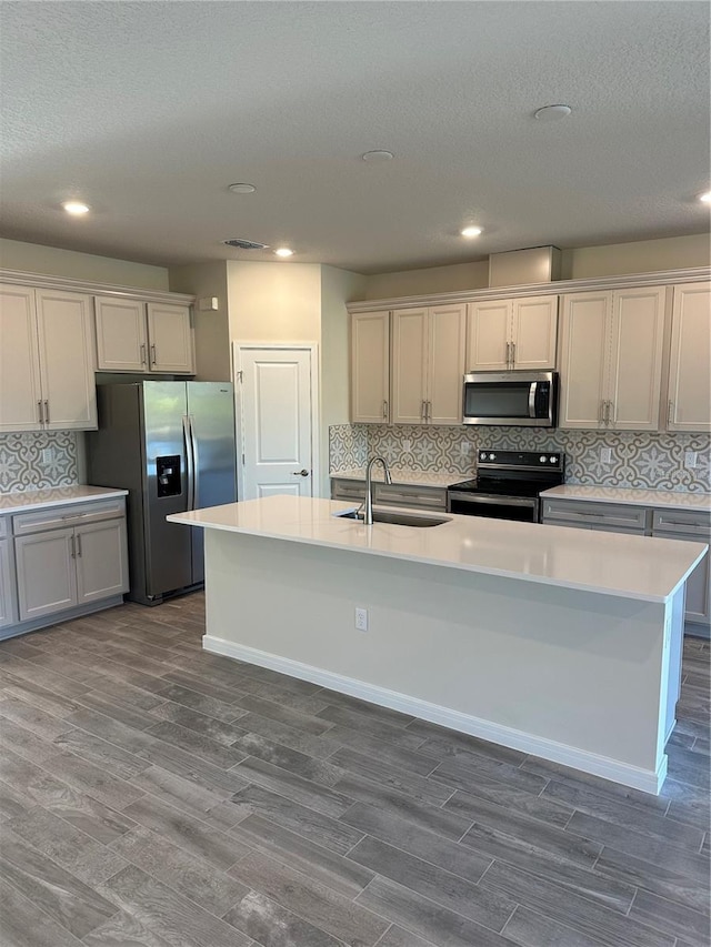 kitchen featuring stainless steel appliances, sink, tasteful backsplash, wood-type flooring, and a center island with sink