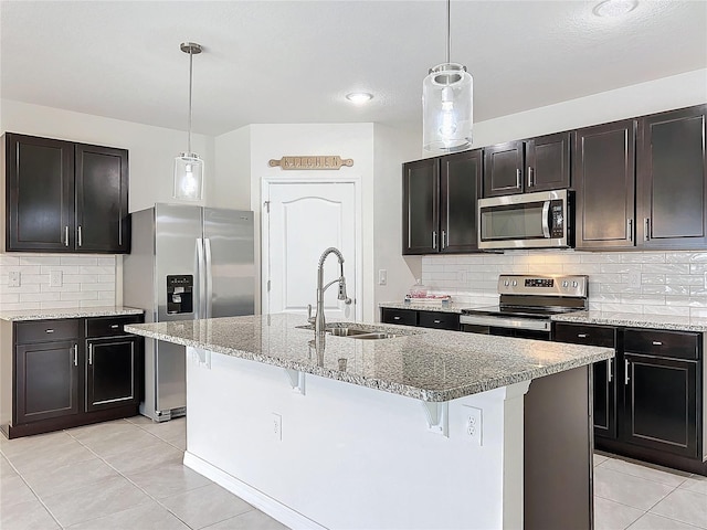 kitchen featuring a kitchen island with sink, stainless steel appliances, hanging light fixtures, light tile patterned floors, and sink