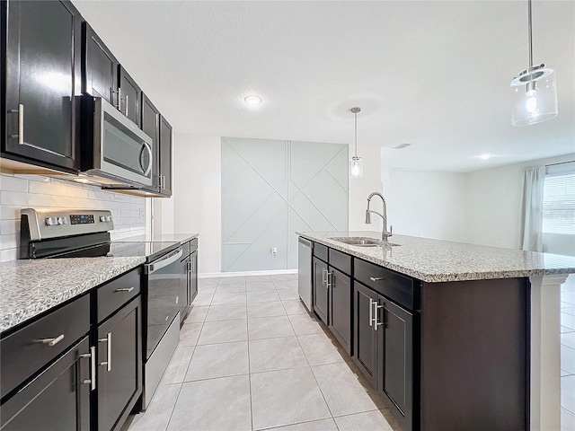 kitchen featuring pendant lighting, light tile patterned floors, a kitchen island with sink, appliances with stainless steel finishes, and sink