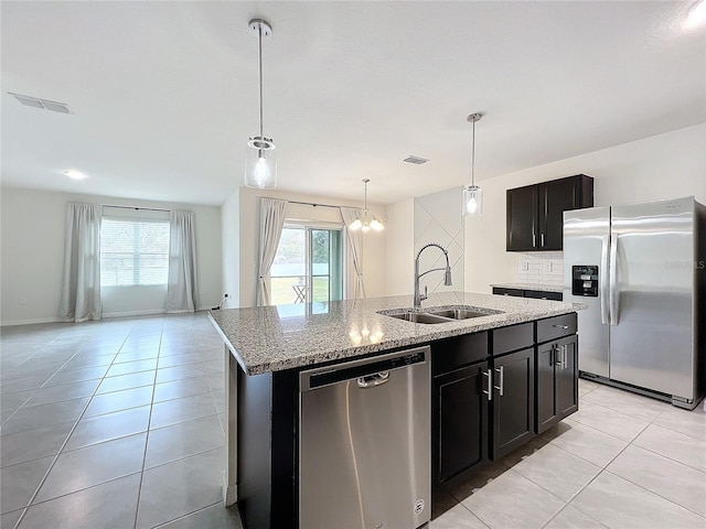 kitchen with sink, an inviting chandelier, light stone counters, a kitchen island with sink, and appliances with stainless steel finishes