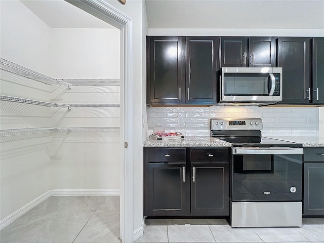 kitchen featuring stainless steel appliances, decorative backsplash, light tile patterned flooring, and light stone countertops