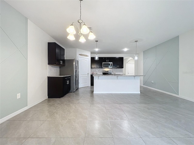 kitchen featuring an island with sink, a notable chandelier, light tile patterned floors, tasteful backsplash, and appliances with stainless steel finishes