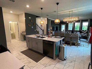 kitchen with sink, black dishwasher, hanging light fixtures, a kitchen island with sink, and a notable chandelier