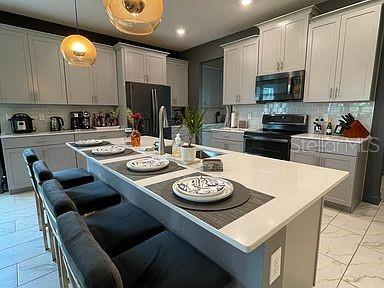 kitchen featuring a breakfast bar, stainless steel fridge, black electric range, and hanging light fixtures