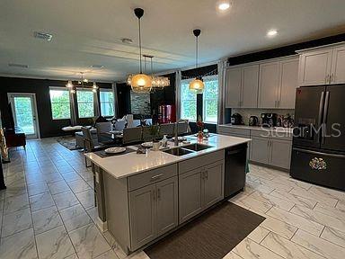 kitchen featuring sink, decorative light fixtures, a center island with sink, black appliances, and gray cabinetry