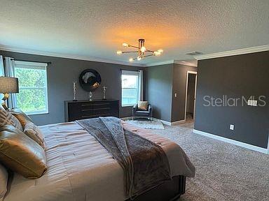 bedroom featuring a textured ceiling, a chandelier, crown molding, and carpet flooring