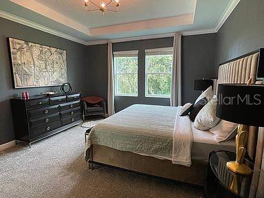 carpeted bedroom featuring a raised ceiling and a chandelier