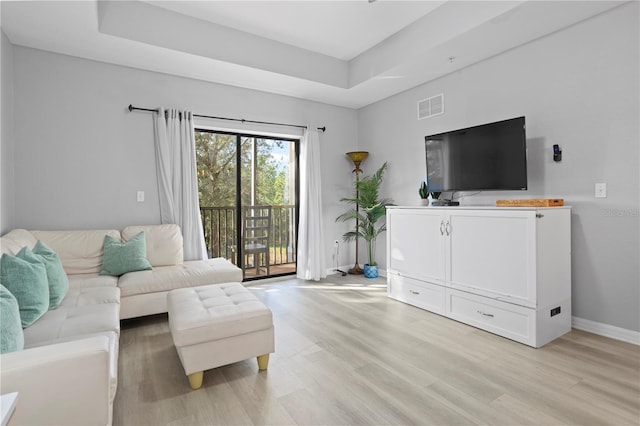 living room with light hardwood / wood-style floors and a raised ceiling