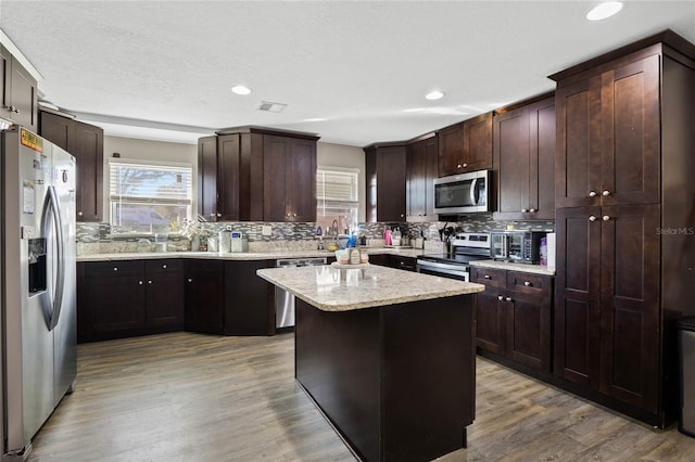 kitchen featuring light stone counters, light hardwood / wood-style floors, a kitchen island, backsplash, and appliances with stainless steel finishes