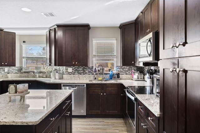 kitchen featuring stainless steel appliances, light wood-type flooring, light stone counters, sink, and dark brown cabinets