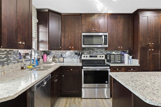 kitchen featuring light stone countertops, appliances with stainless steel finishes, light hardwood / wood-style flooring, and sink